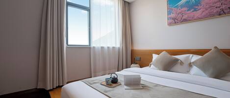 Ein Hotelzimmer mit einem großen Bett, einem Fenster mit Vorhängen, einem Gemälde vom Fuji und einem Nachttisch mit Wasserkocher und Tasse.