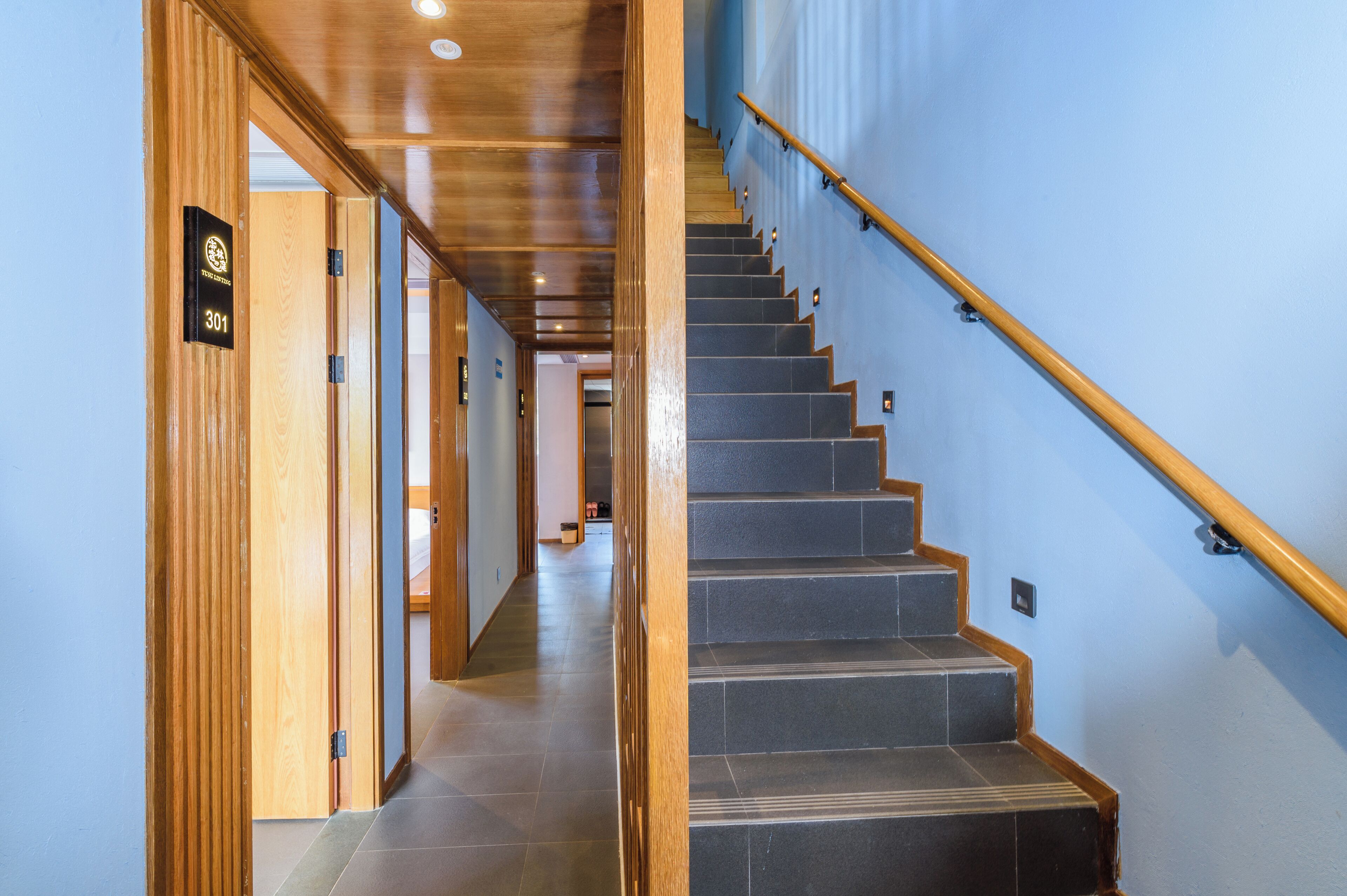 A wooden hallway leading to a staircase with a blue wall and a wooden handrail.