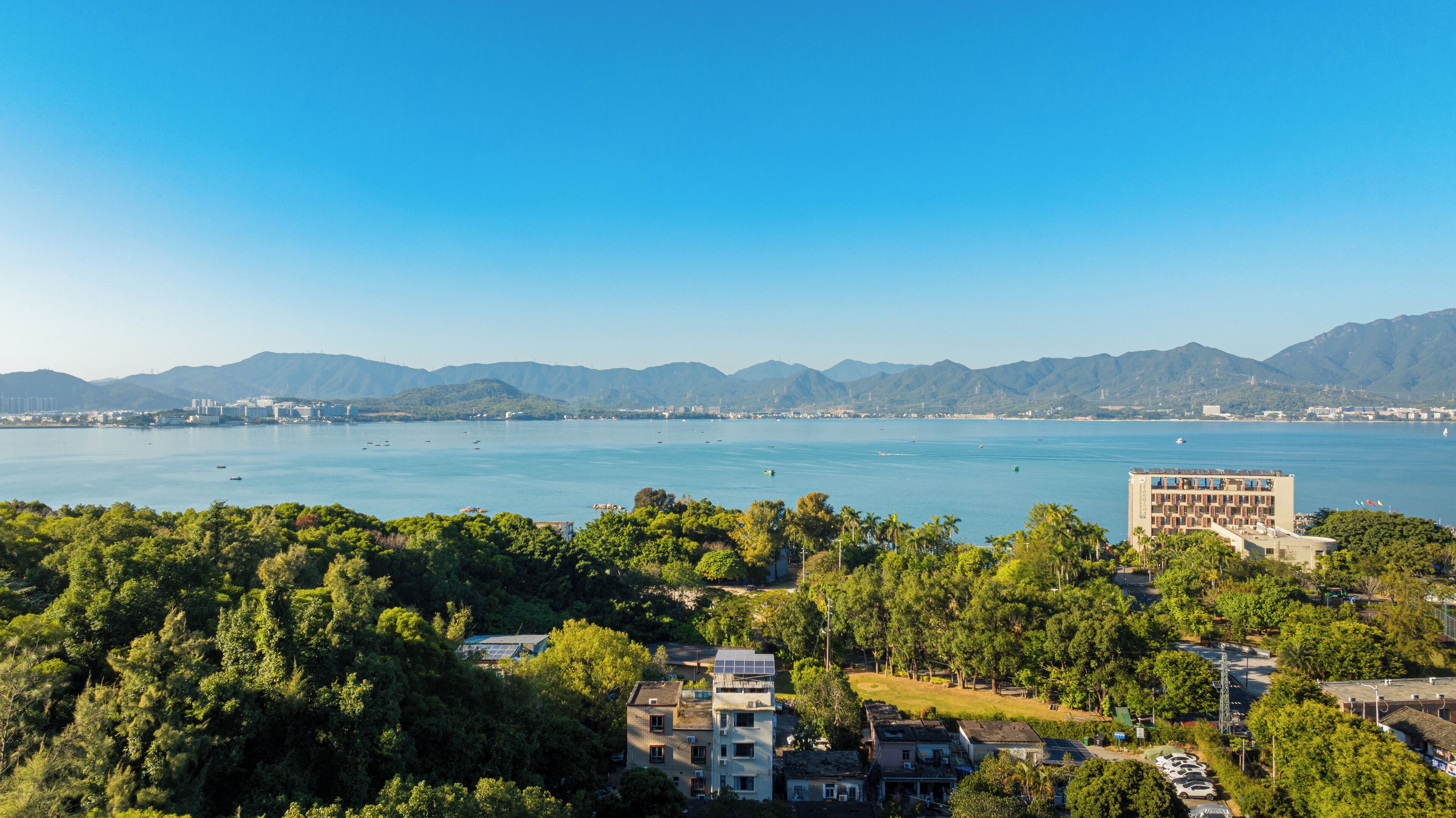 A coastal cityscape with a view of the sea, mountains in the background, and a mix of residential and commercial buildings.