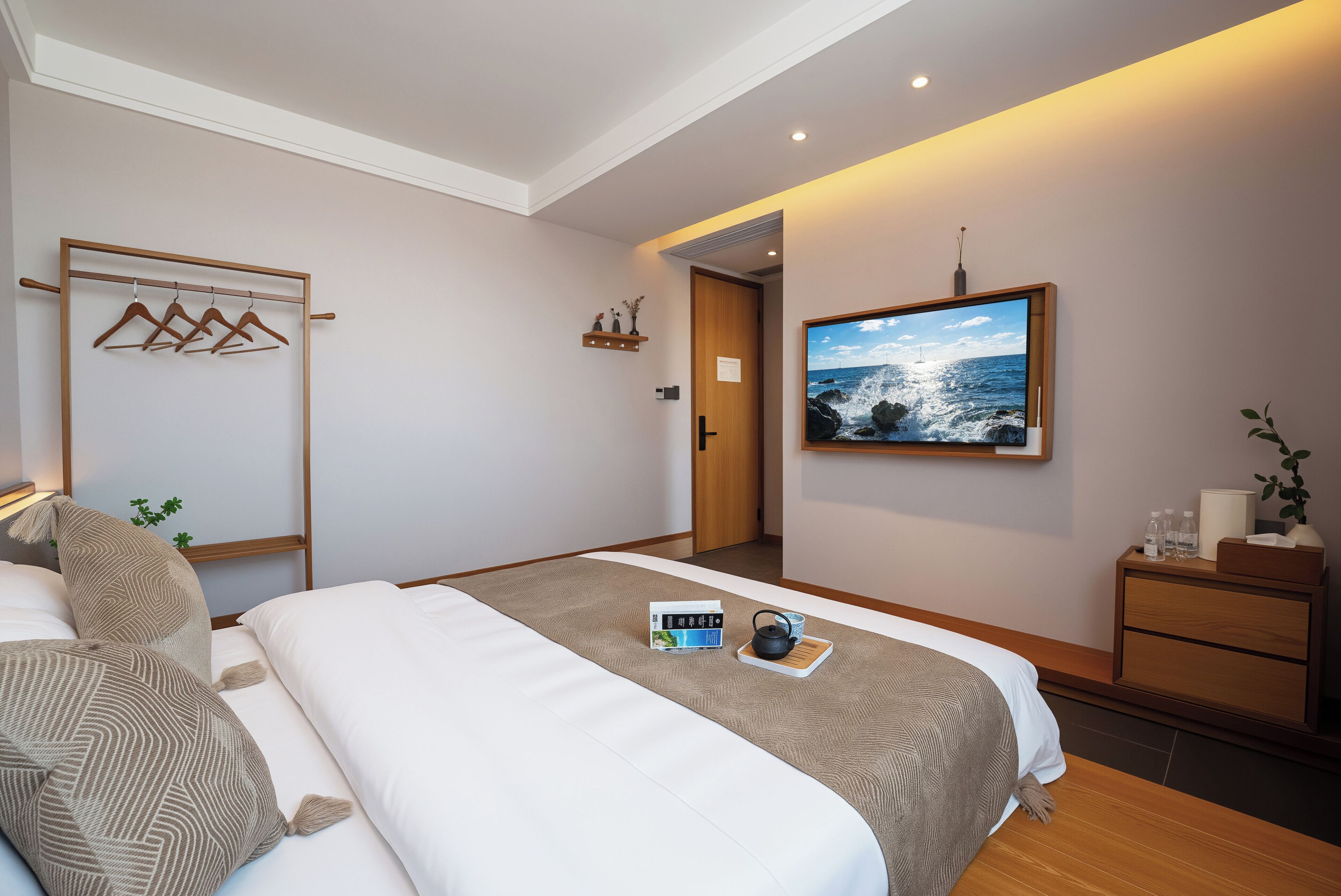 Quarto de hotel moderno com uma cama grande, televisão de tela plana, cômoda de madeira e vista para o oceano.