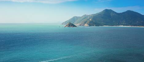 A coastal landscape with mountains, clear skies, and calm sea.