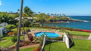 A pool area with a view of the ocean, surrounded by greenery and palm trees.