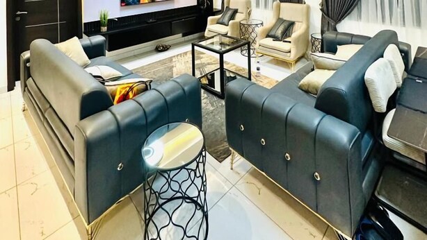 A modern living room with a flat-screen TV, leather sofas, a coffee table, and a ceiling light fixture. - Mankatiwa Court Apartmentnt (Weija)