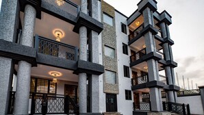A multi-story building with a modern architectural design, featuring prominent columns, balconies, and a mix of stone and glass materials. - Mankatiwa Court Apartmentnt (Weija)
