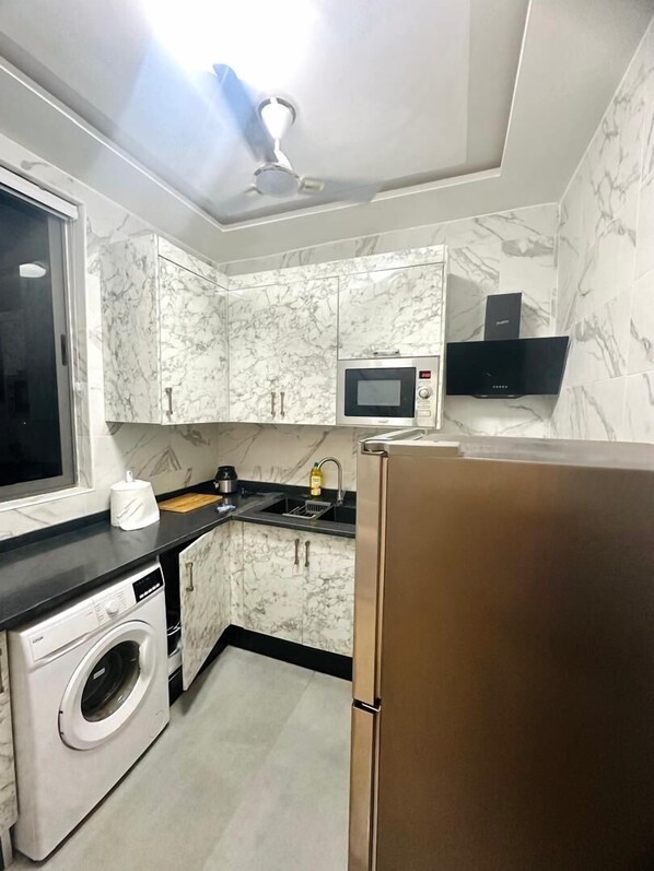 A compact kitchen with marble cabinets, a built-in microwave, a washing machine, and a refrigerator.