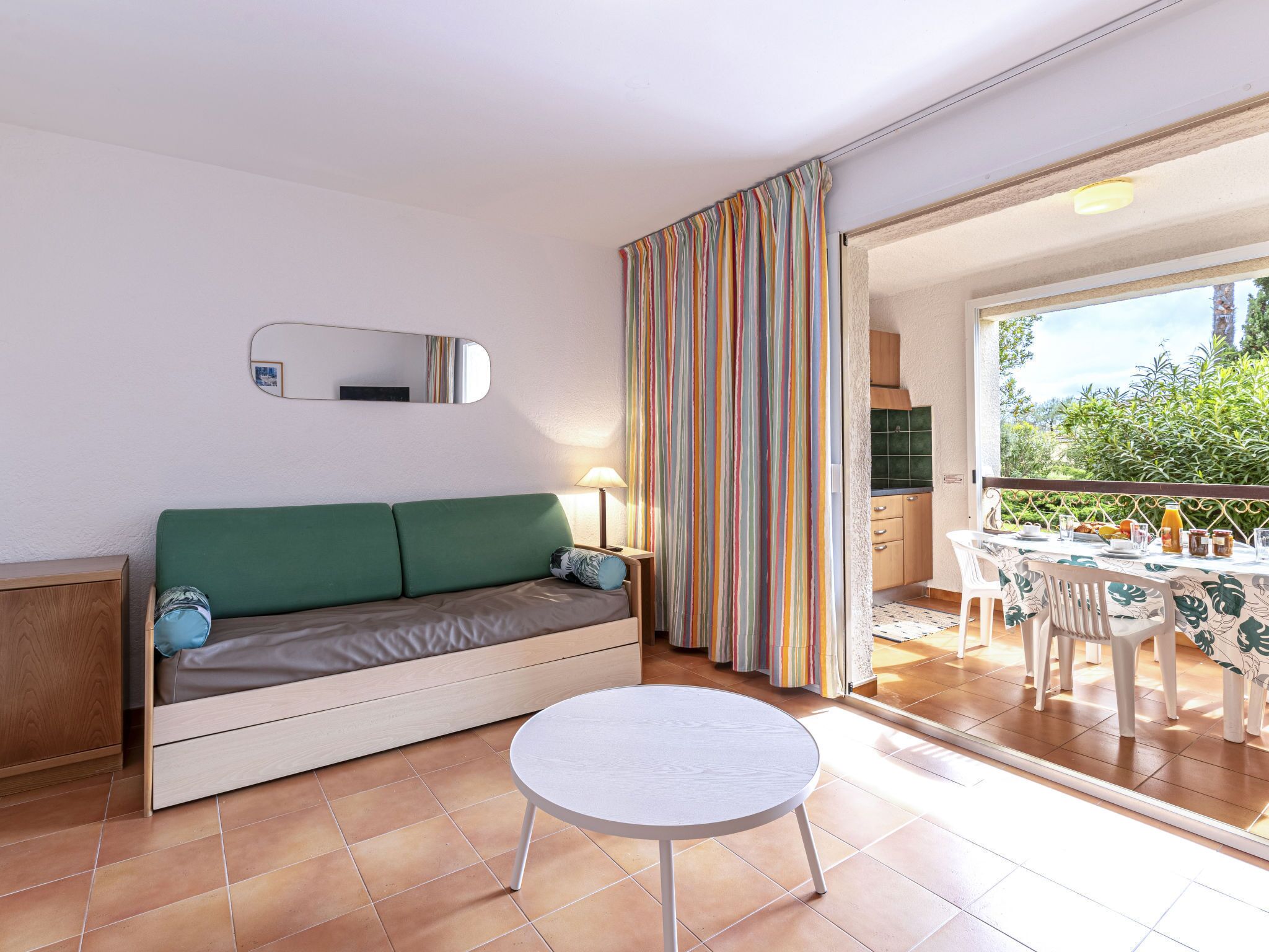 A room with a green sofa, a round table, a mirror, and a view of the outdoors.