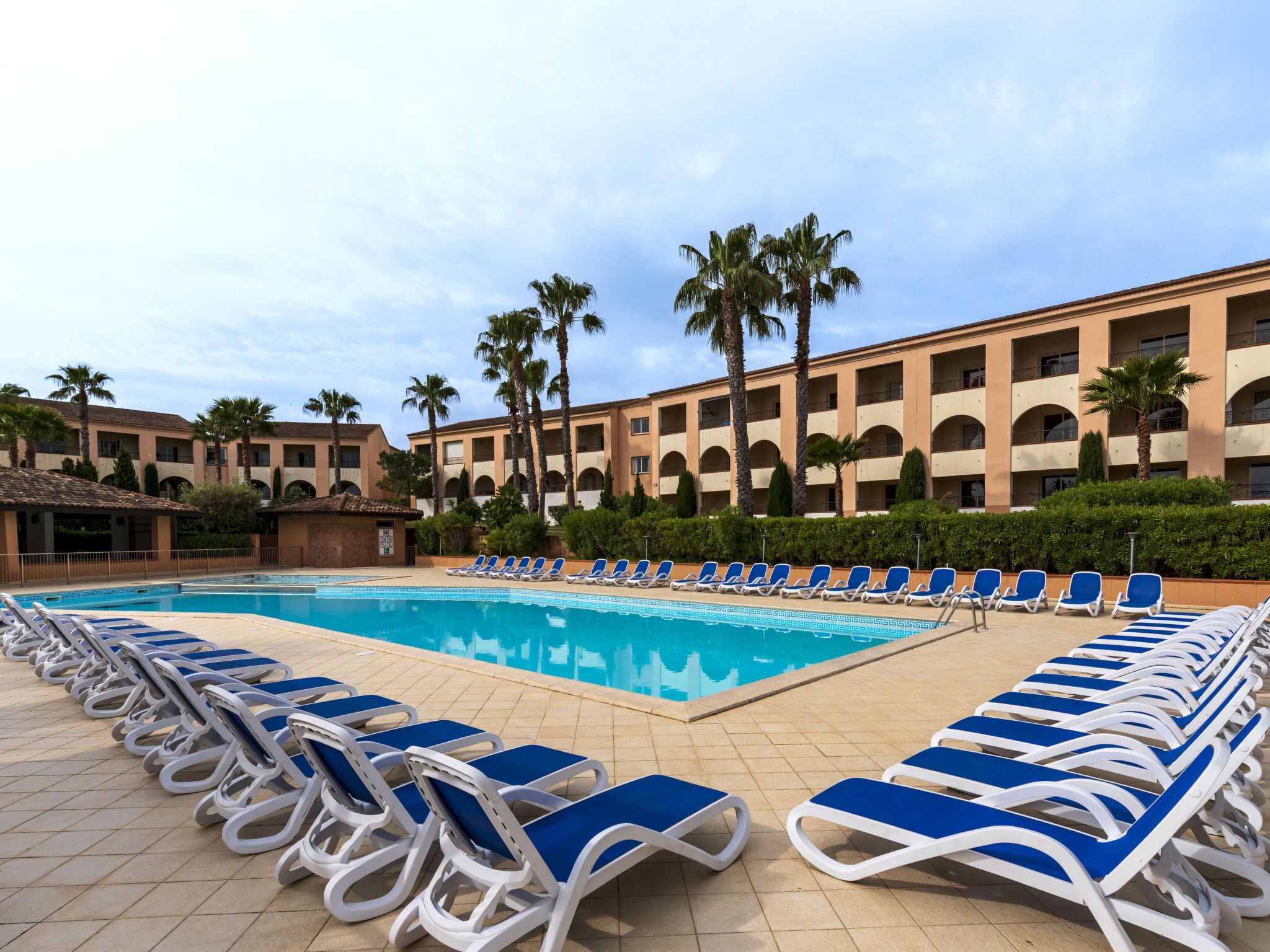 A pool area with blue lounge chairs and a building with multiple balconies.