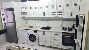 A compact kitchen with white cabinets, a stainless steel refrigerator, a washing machine, a sink, and a stove. - Hibe Dede Hotel Cappadocia (Nevşehir)