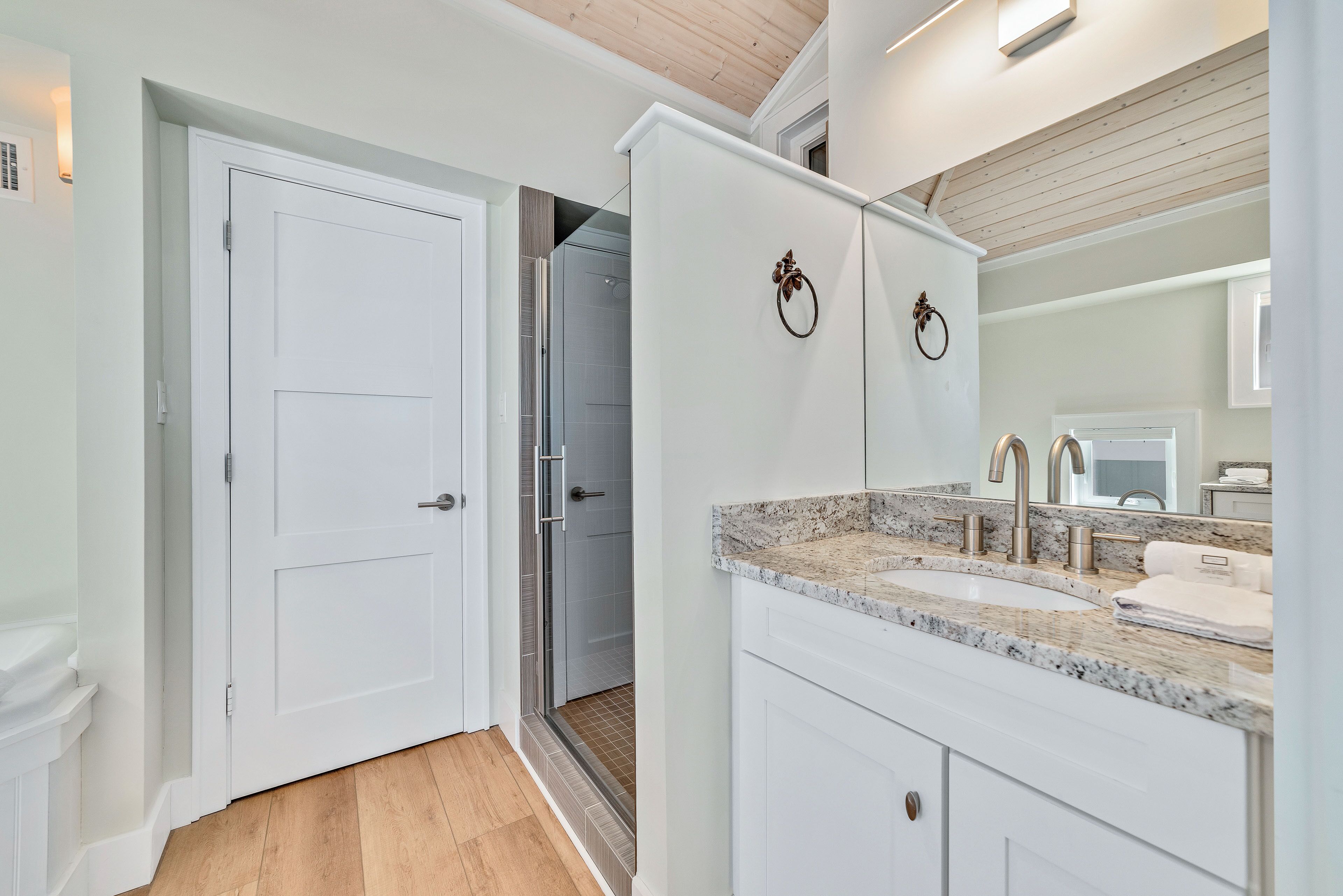 A modern bathroom with a white door, a shower area, and a granite countertop with a sink.