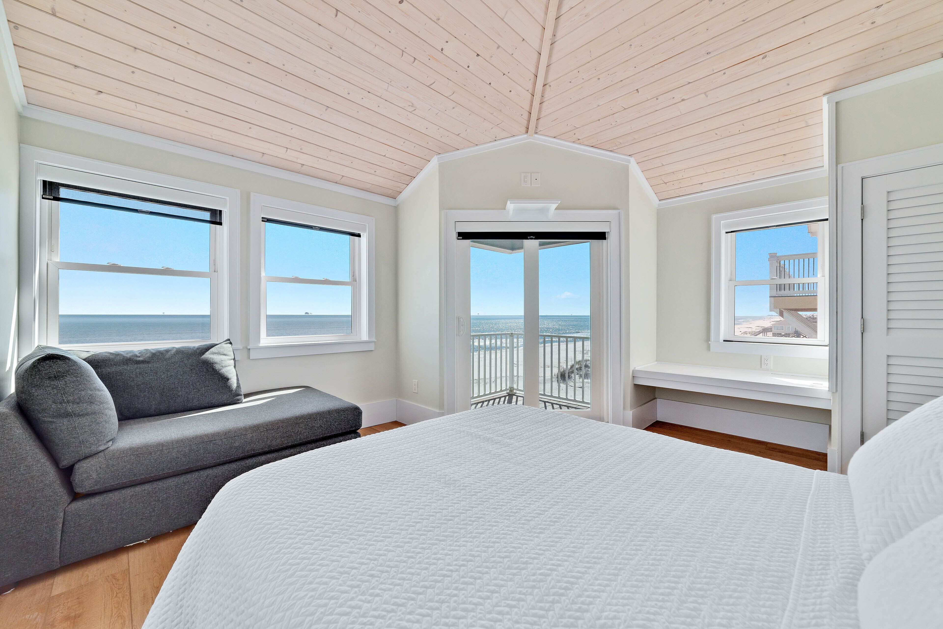 Een slaapkamer met een groot bed, een grijze bank en een raam met uitzicht op de oceaan.