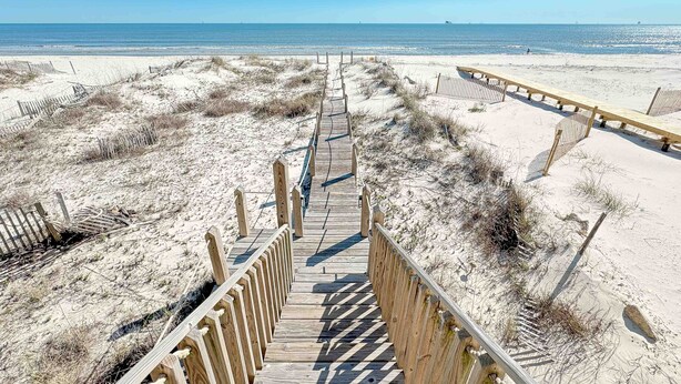 A wooden boardwalk leading to a beach with sandy dunes and a clear blue sky.