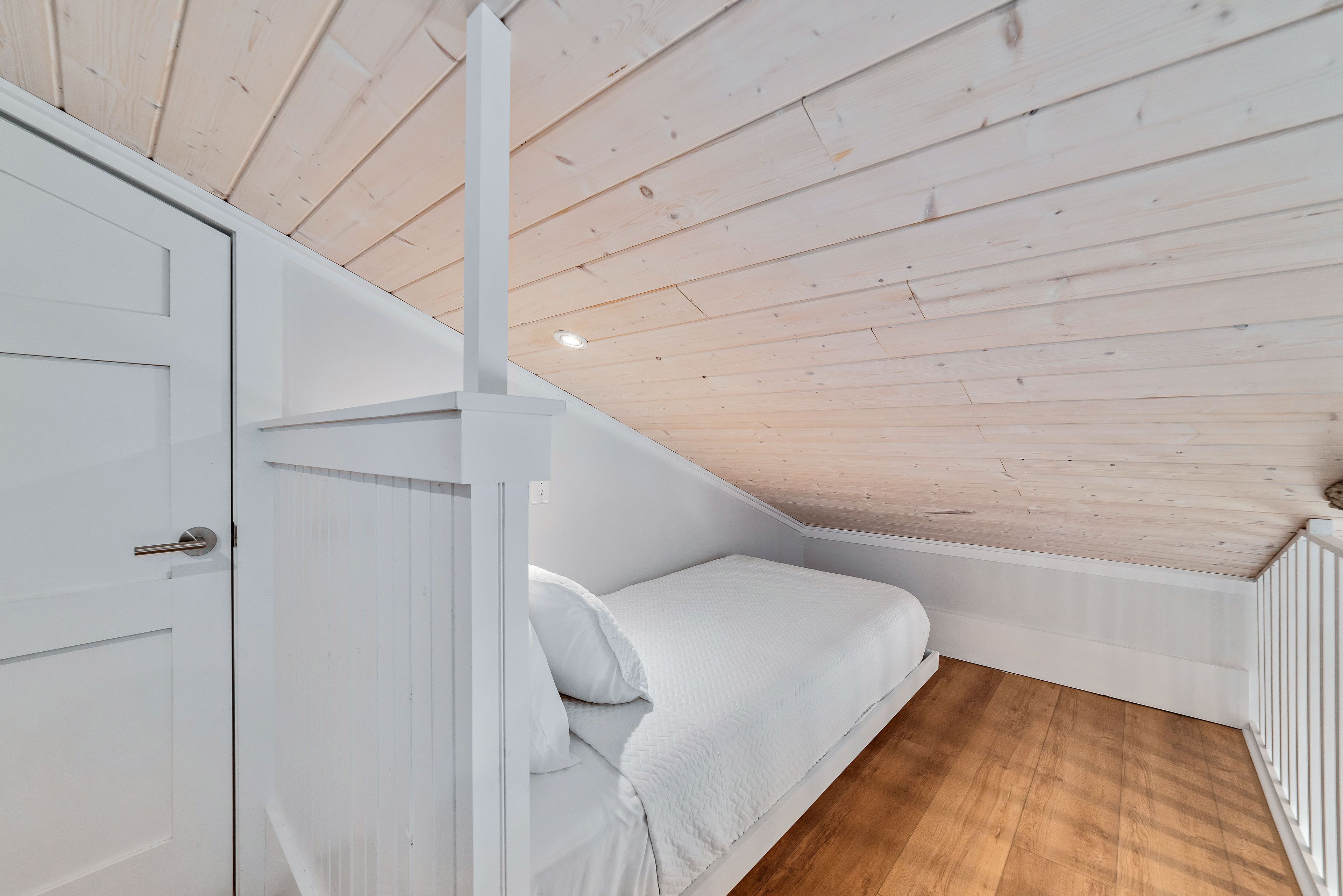Una habitación pequeña con cama individual, techo inclinado y suelo de madera.