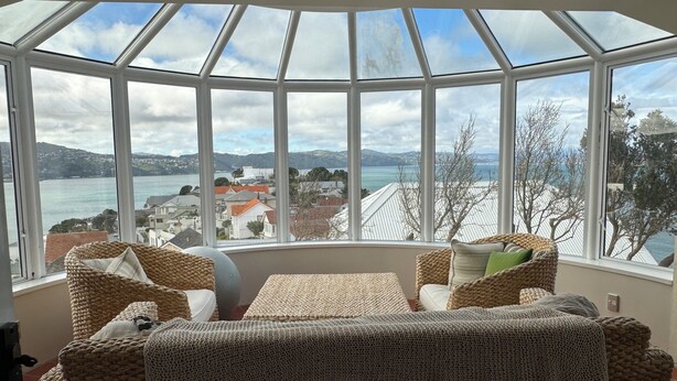 A room with a large bay window overlooking a coastal view, featuring wicker furniture and a knitted throw. - Super large seaview house (Wellington)