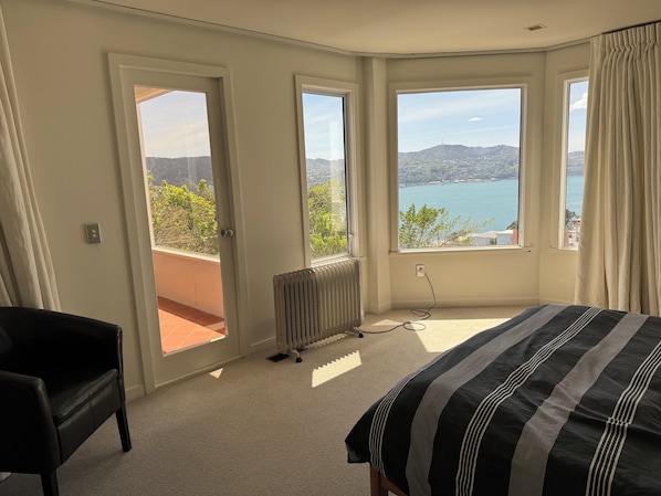 Une chambre à coucher comprenant un lit, une chaise et de grandes fenêtres donnant sur un plan d’eau et des collines.