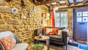 A cozy room with a stone wall, a sofa, a chair, a small round table, and a window with curtains. - Maison du Bosco by Interhome (Auray)