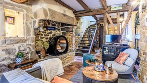 A rustic interior with a stone fireplace, wooden beams, a sofa, a television, and a staircase leading to another level. - Maison du Bosco by Interhome (Auray)
