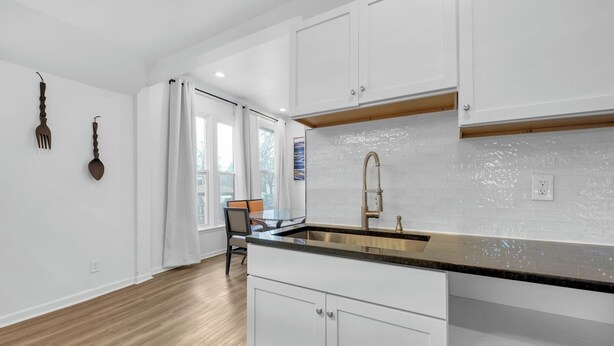 A modern kitchen with white cabinetry, a stainless steel sink, and a dining area with a table and chairs. - Detroit 3BR in Mexicantown | Sleeps 7 + WiFi (Detroit)