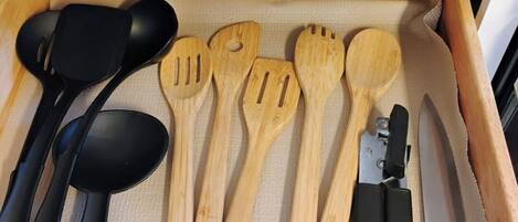 A drawer containing various kitchen utensils, including black and wooden spoons, spatulas, and a knife.