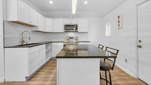 A modern kitchen with white cabinetry, a central island, stainless steel appliances, and a pendant light. - Detroit 3BR in Mexicantown | Sleeps 7 + WiFi (Detroit)