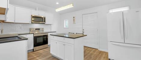 Una cocina moderna con muebles blancos, horno de acero inoxidable, microondas y refrigerador.