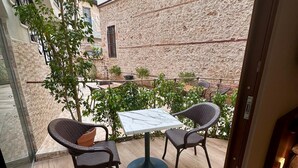 An outdoor patio with a table and two wicker chairs, a stone wall, and a tree. - Adria Inn (Antalya)