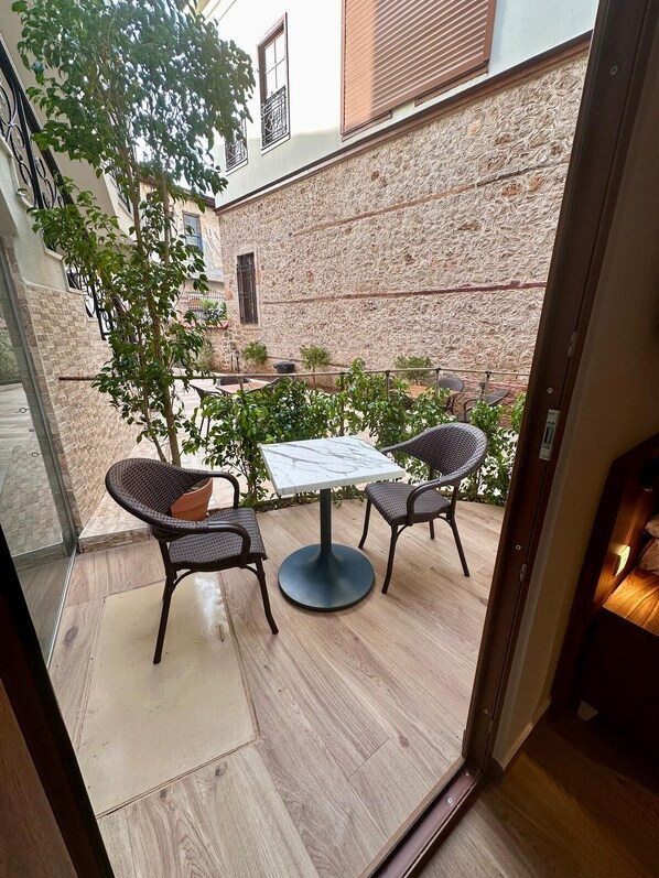 An outdoor patio with a table and two wicker chairs, a stone wall, and a tree. - Adria Inn (Antalya)