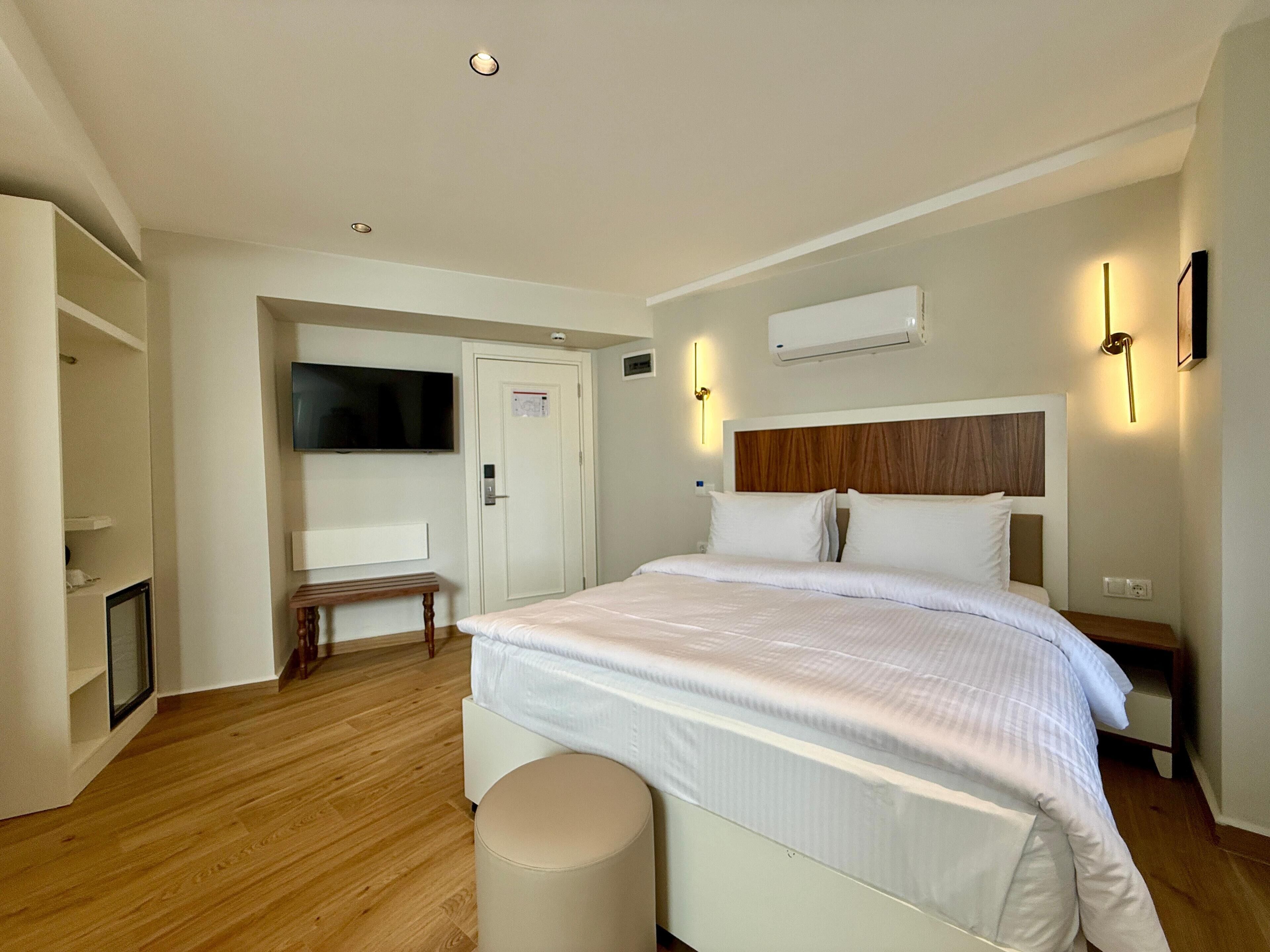 A modern hotel room with a large bed, a television, a desk, and a chair.
