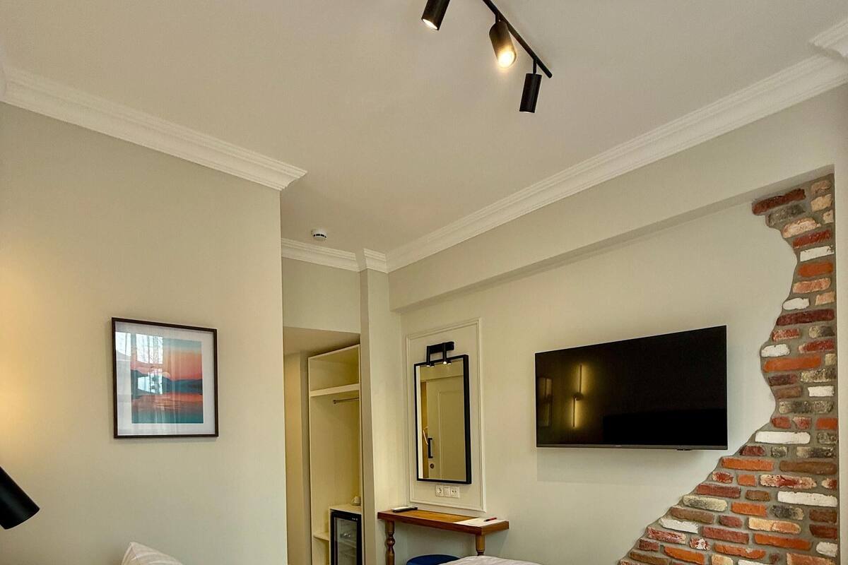 A hotel room with a large bed, a flat-screen TV mounted on the wall, a brick accent wall, and a ceiling light fixture.
