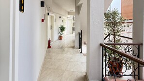 A corridor with a tiled floor, a fire extinguisher, a potted plant, and a balcony with a wrought iron railing. - Adria Inn (Antalya)