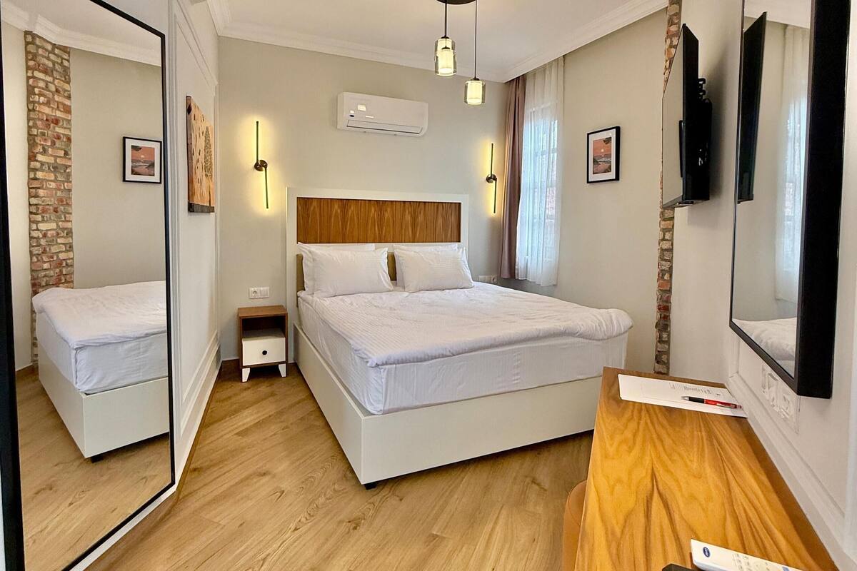 A hotel room with a large bed, a wooden desk, a TV, and a mirror.