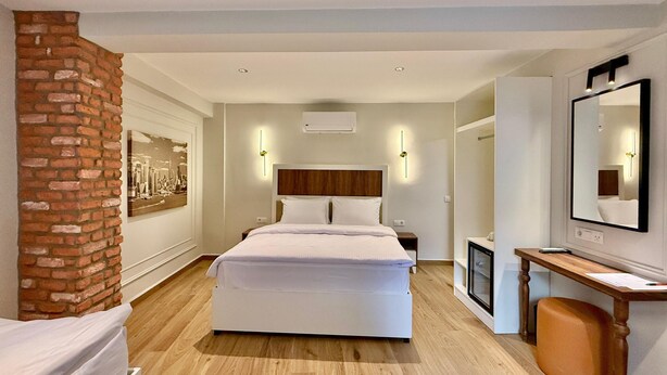 A modern hotel room with a large bed, a wooden floor, a brick accent wall, a desk with a chair, and a large mirror. - Adria Inn (Antalya)