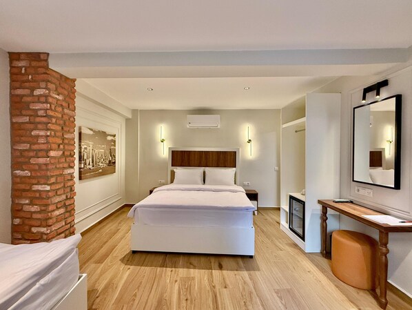 A modern hotel room with a large bed, a wooden floor, a brick accent wall, a desk with a chair, and a large mirror.