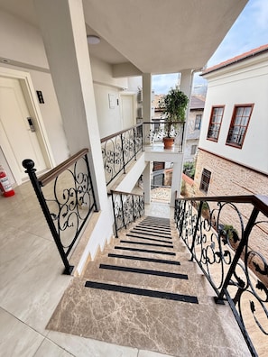 Ein mehrstöckiges Wohngebäude mit einer Marmortreppe, Metallgeländern und einem Blumentopf auf dem Balkon.