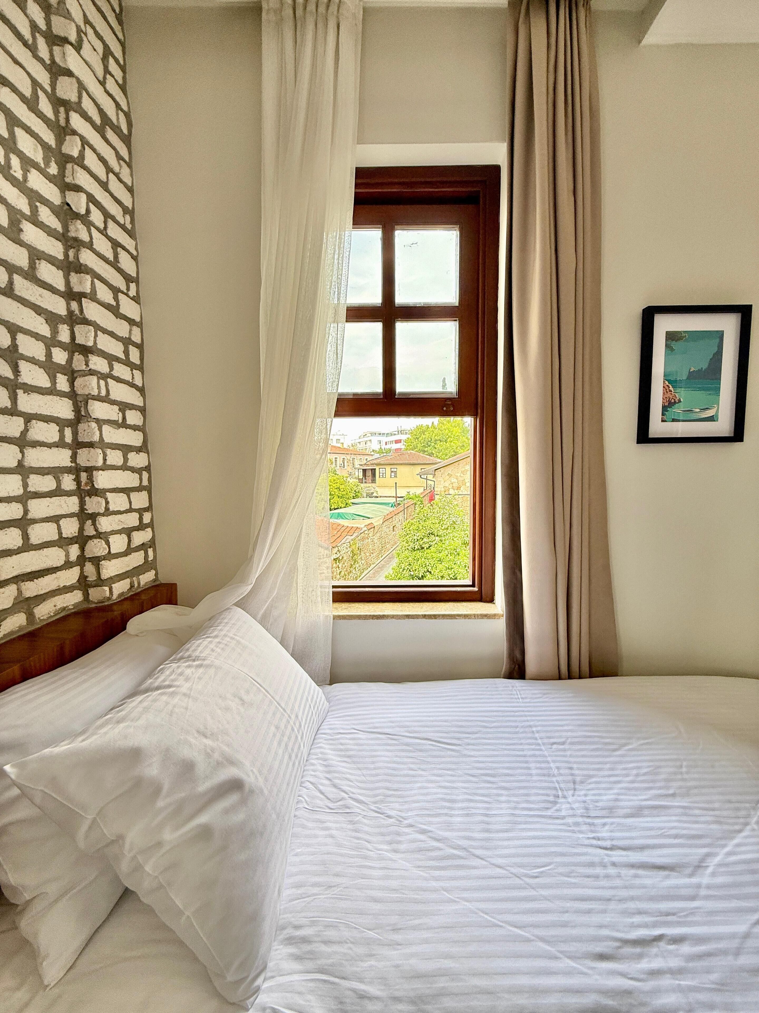 Un dormitorio con cama, una ventana con cortinas, una pared de ladrillo y un cuadro enmarcado en la pared.