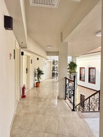 A corridor with a fire extinguisher, potted plants, and a staircase with a railing.