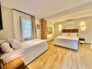 A hotel room with a bed, a sofa, a brick accent wall, and a cityscape painting.