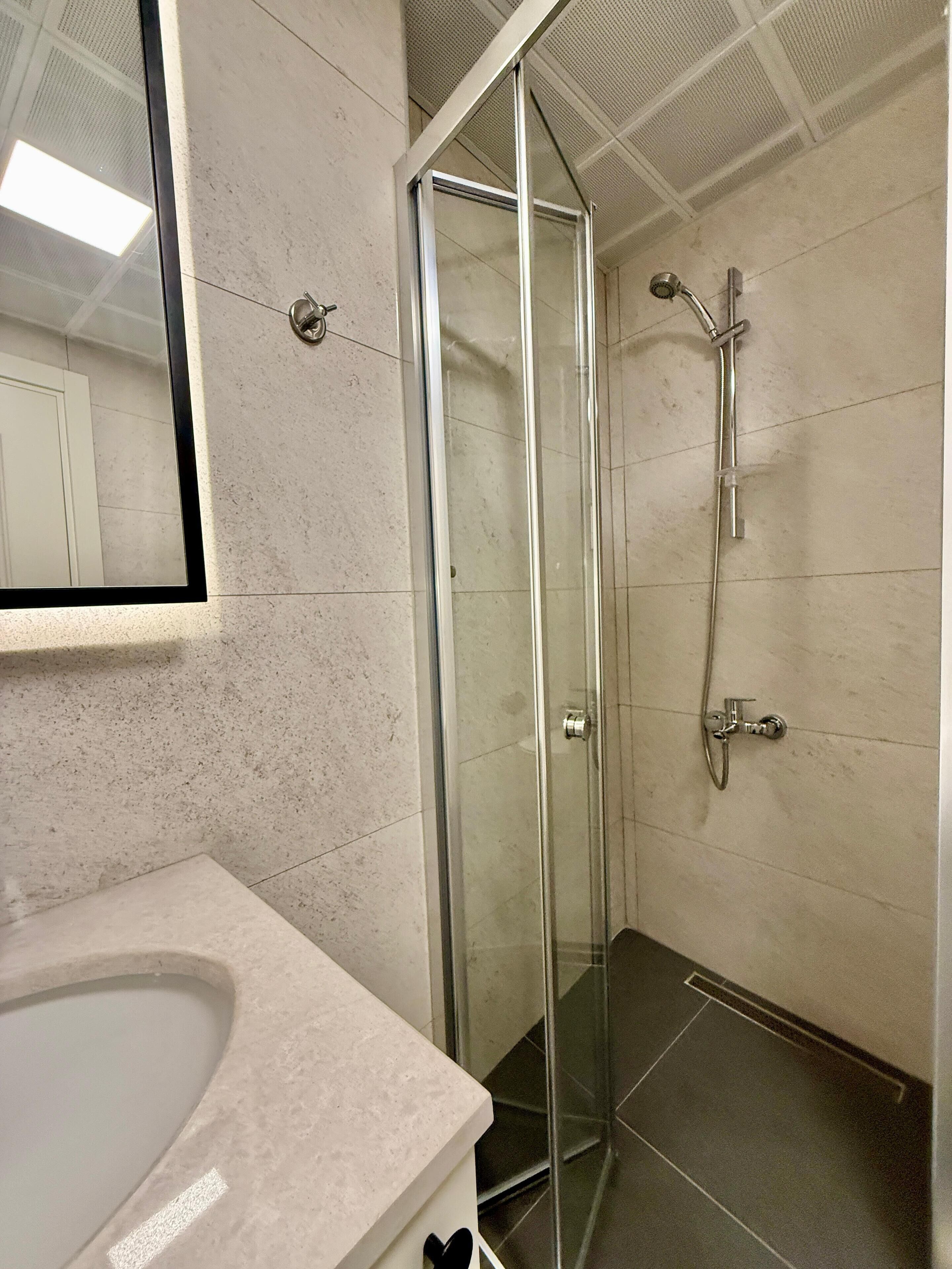A bathroom with a glass shower enclosure, a sink with a mirror, and tiled walls.