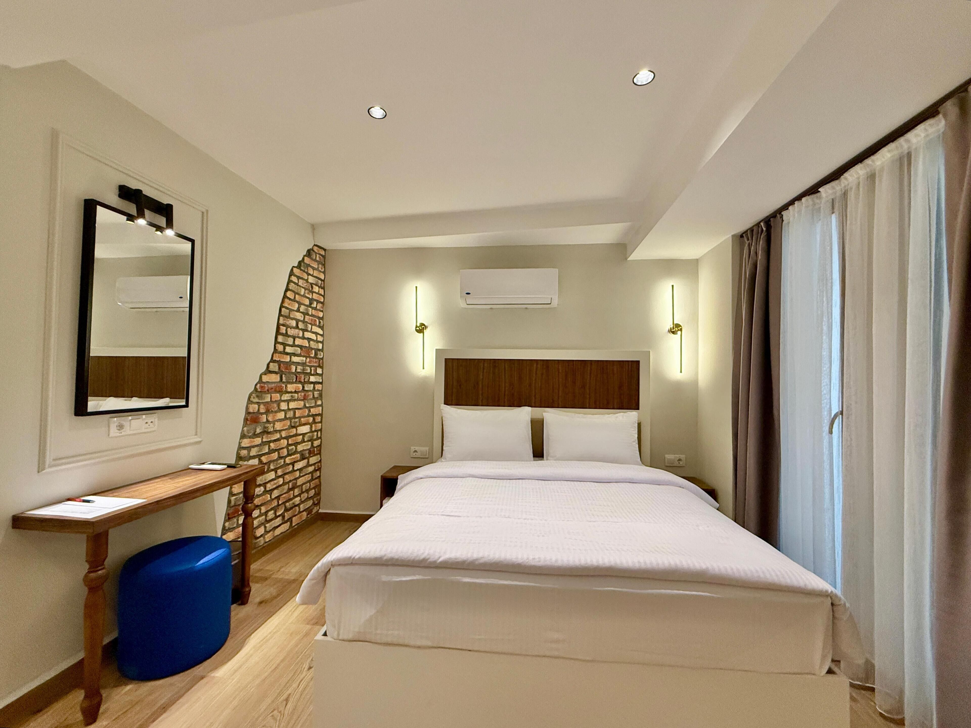 A hotel room with a bed, a desk, a mirror, and a brick accent wall.
