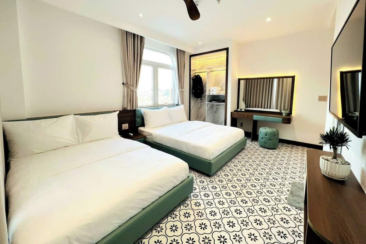 A hotel room with two beds, a desk, a mirror, and a ceiling fan.