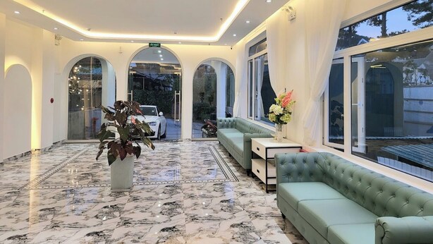A lobby with a marble floor, green upholstered seating, a potted plant, and a view of the outside.