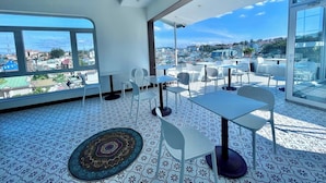A modern rooftop terrace with white furniture, patterned floor tiles, and large windows offering a city view.