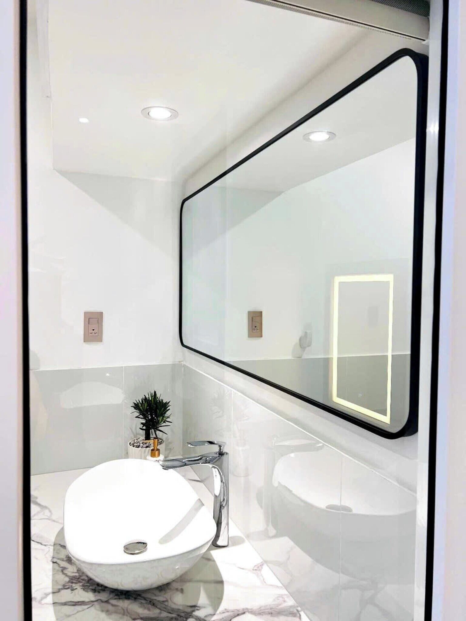 Une salle de bain moderne avec un grand miroir, un lavabo blanc et un sol en marbre.