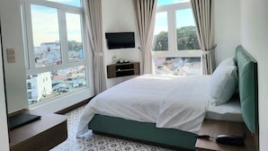 A modern hotel room with a large bed, a ceiling fan, a TV, and a view of the city.
