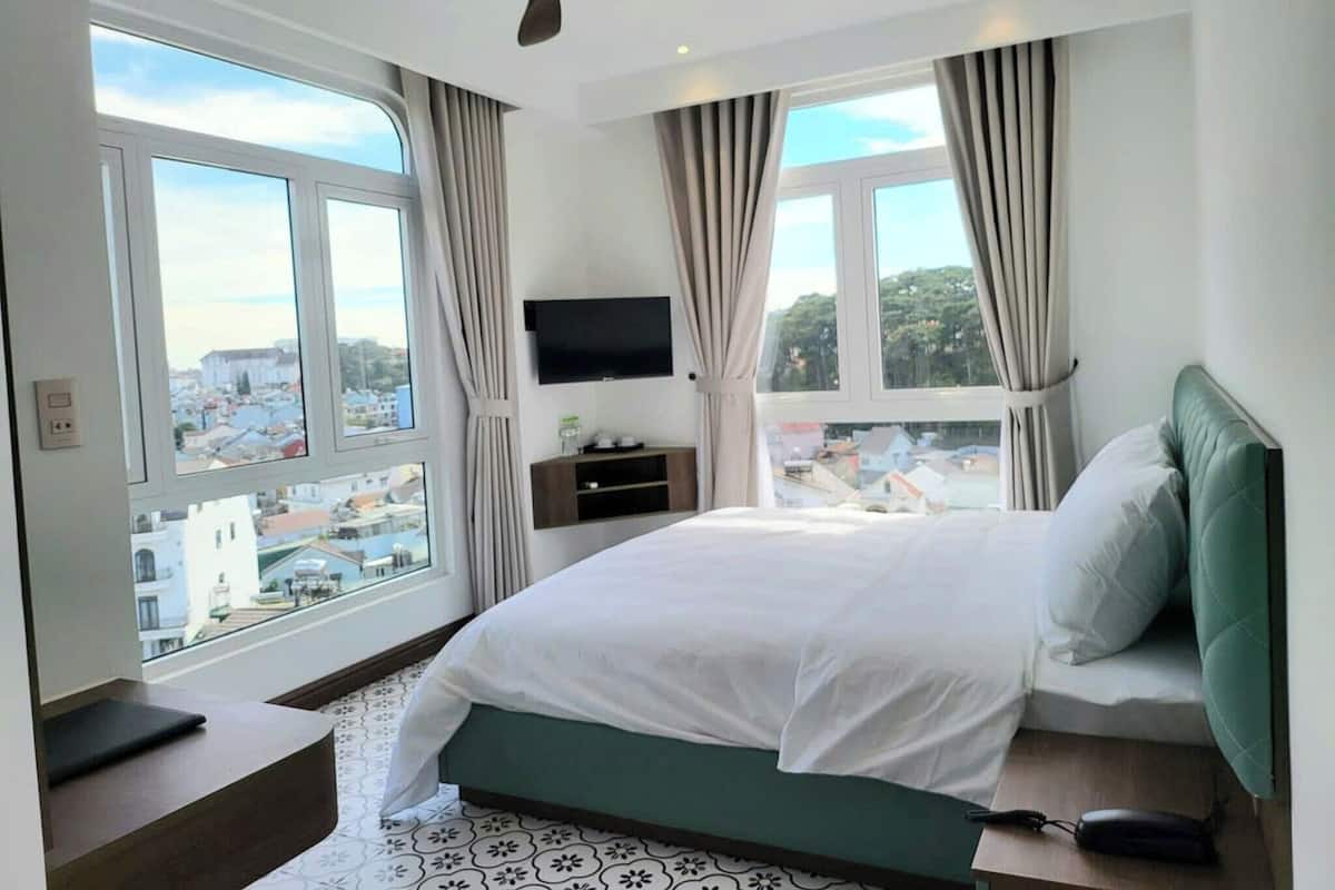 A modern hotel room with a large bed, a ceiling fan, a TV, and a view of the city.