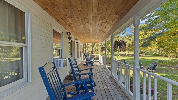 Eine überdachte Veranda mit blauen Adirondack-Stühlen, weißen Geländern und einer Holzzieldecke.