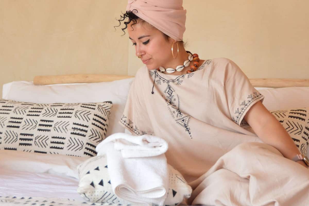 A person sitting on a bed with patterned pillows and a white blanket.