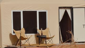 Relax in this desert retreat with a large window and door for natural light and ventilation, featuring two chairs and a small table for a peaceful space.