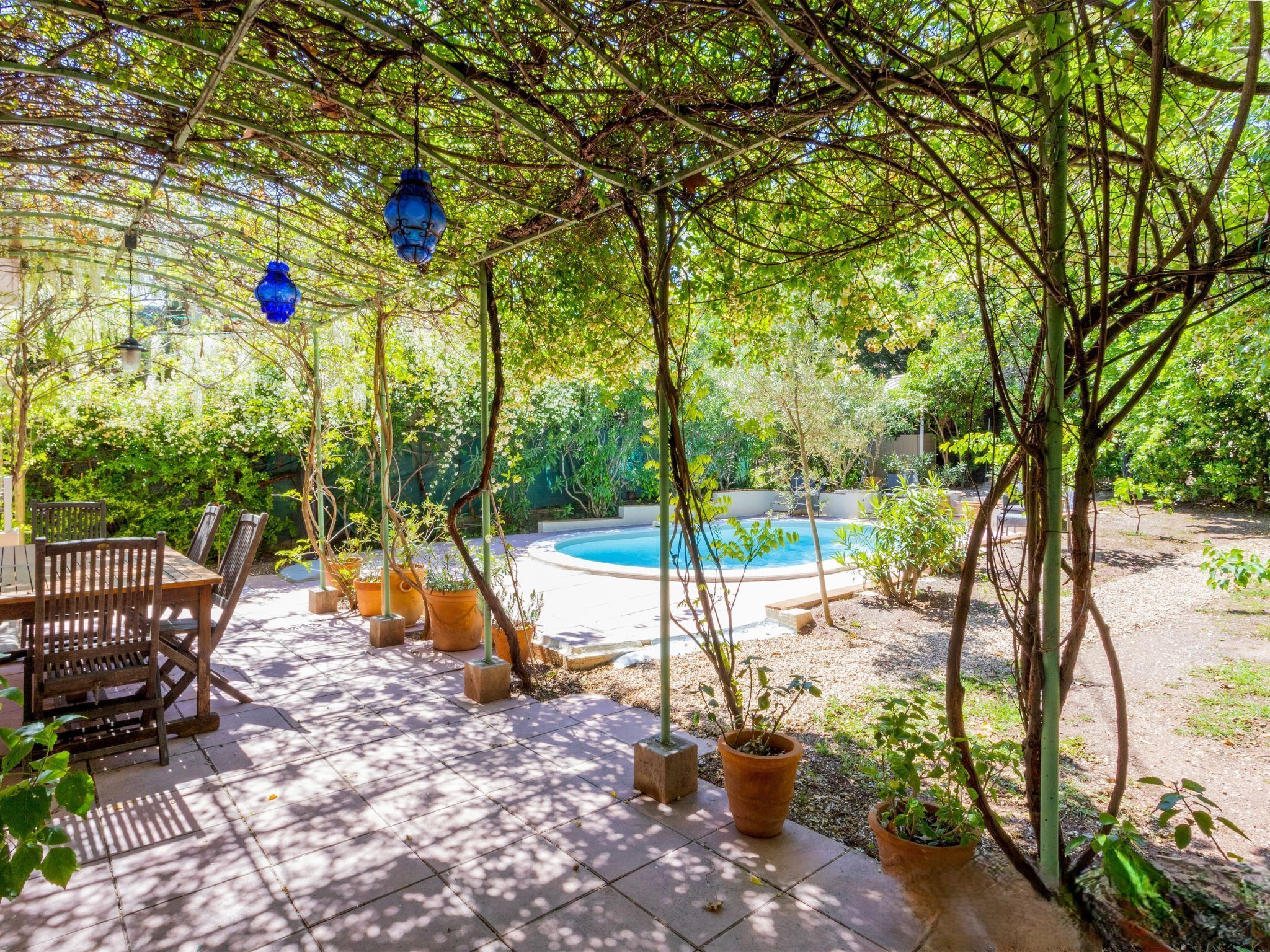 Un patio couvert avec une piscine, des meubles en bois et des plantes en pot.