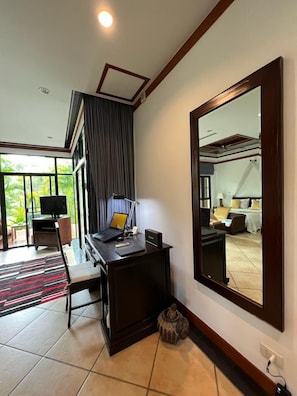 A hotel room with a large mirror, a desk with a laptop, a television, and a view of the outdoors.