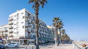 Een meerhoog hotel met balkons, een winkel op de begane grond en palmbomen langs de straat.